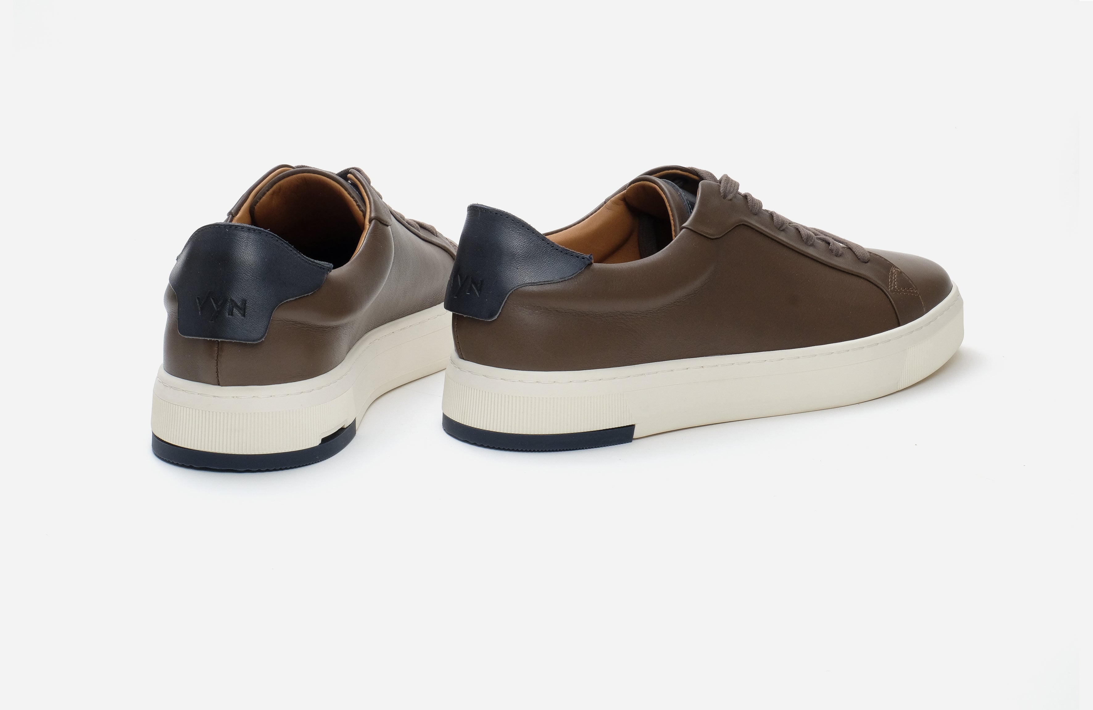 Pair of brown sneakers with white soles on a light gray background